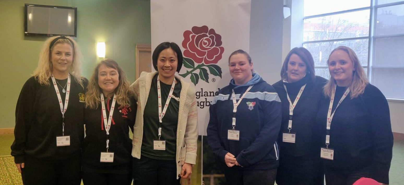 NLD's 6 representatives at the conference smiling for the camera in front of an England rugby banner.